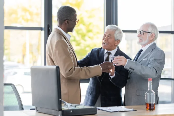 Happy senior business partners clinking glasses near contract and briefcase with money — Stock Photo