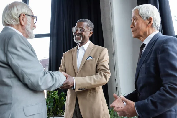 Senior asiatischer Geschäftsmann schaut Geschäftspartnern beim Händeschütteln im Büro zu — Stockfoto
