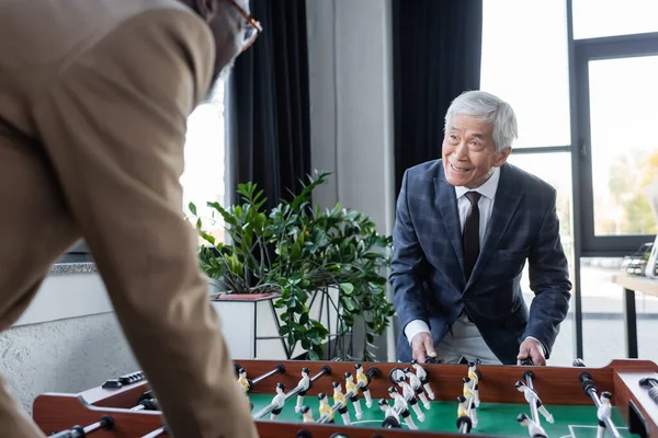 Blurred african american businessman playing table football with senior asian colleague — Stock Photo