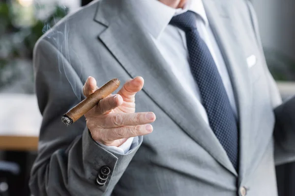 Partial view of senior businessman in suit holding cigar in office — Stock Photo