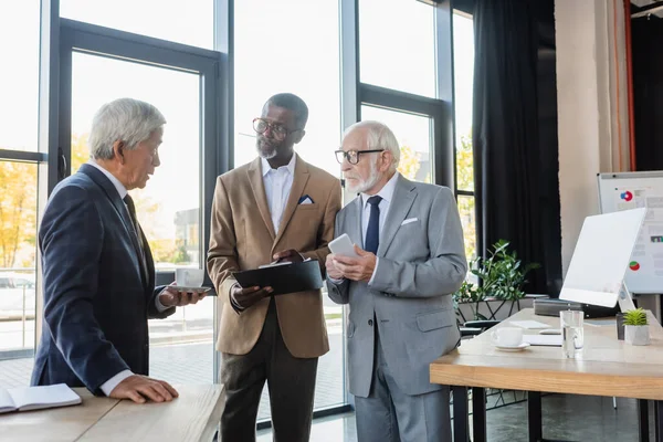 Hombres de negocios multiétnicos mayores discutiendo contrato en el cargo - foto de stock