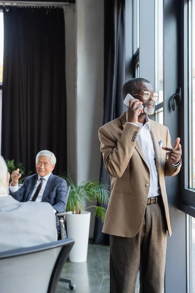 Senior african american businessman talking on cellphone near colleagues working on blurred background — Stock Photo