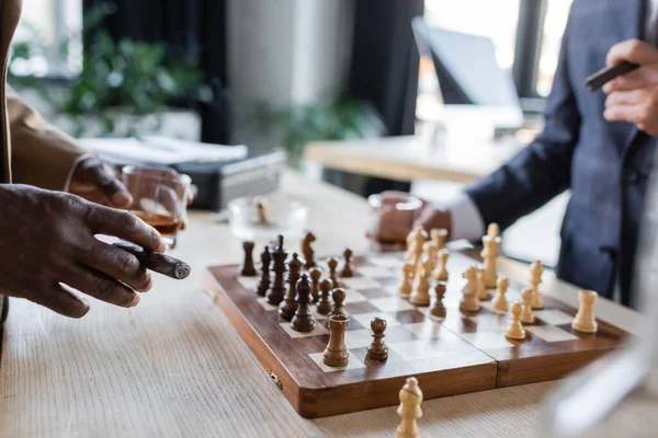 Partial view of businessmen with cigars and glasses of whiskey playing chess in office — Stock Photo