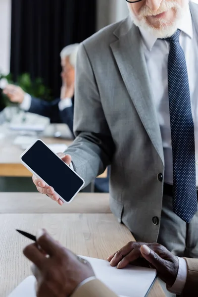 Cropped view of senior businessman showing smartphone with blank screen to african american colleague — Stock Photo