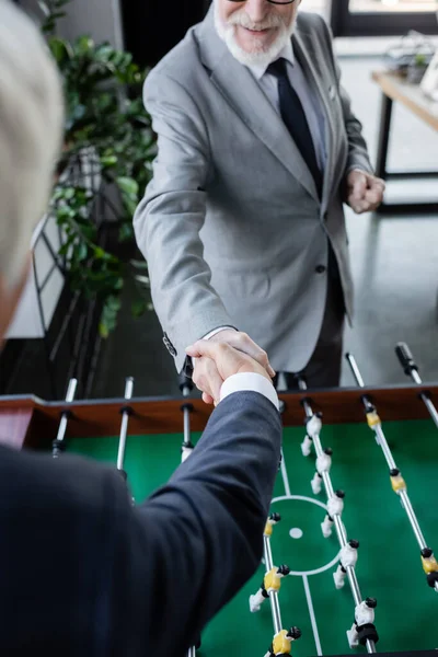 Vista ritagliata di anziano uomo d'affari stringere la mano con collega offuscata vicino calcio balilla — Foto stock