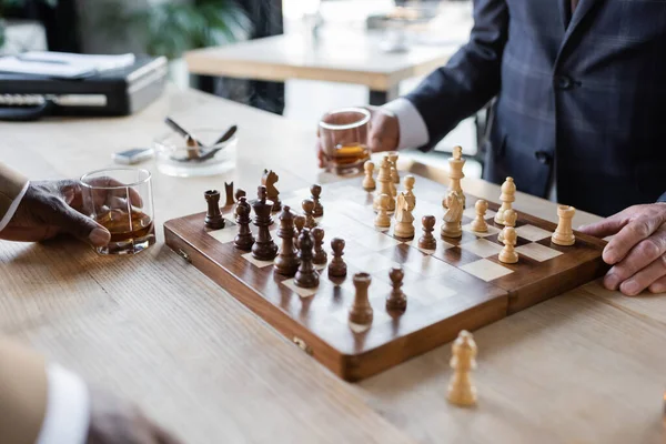 Частковий вид на бізнес-партнерів з келихами віскі, які грають в шахи в офісі — стокове фото