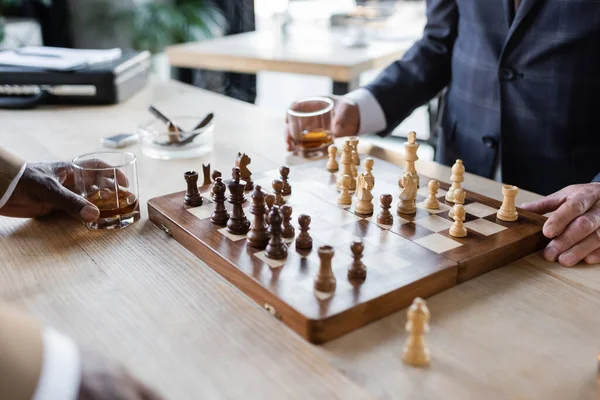 Vue partielle des partenaires commerciaux avec des verres de whisky jouant aux échecs au bureau — Photo de stock