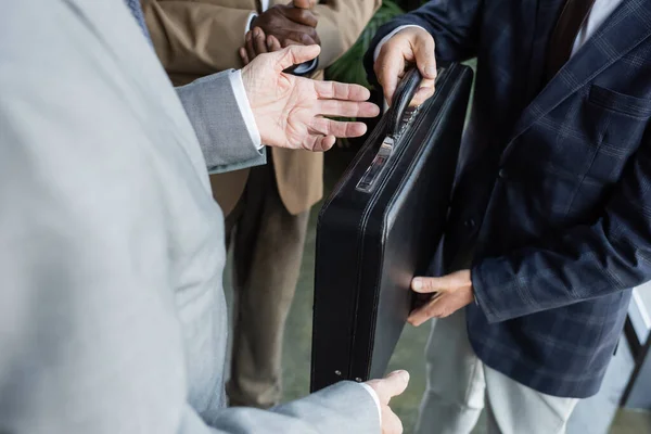 Cropped view of man giving briefcase to multiethnic business partners — Stock Photo
