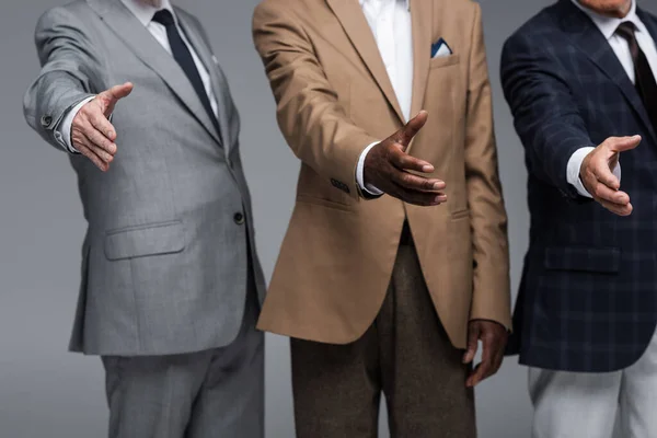Vista recortada de empresarios multiétnicos de alto nivel con las manos extendidas aisladas en gris - foto de stock