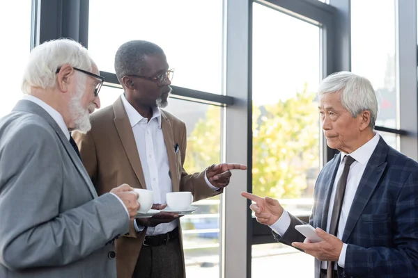Старшие бизнесмены, указывающие пальцами во время дискуссии о кофе-брейке — стоковое фото