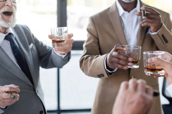 Vue recadrée de l'homme d'affaires sénior excité près de collègues flous avec des verres de whisky — Photo de stock