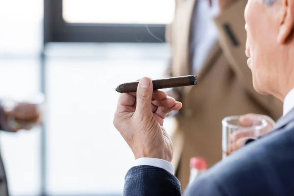 Cropped view of senior businessman smoking cigar in office — Stock Photo