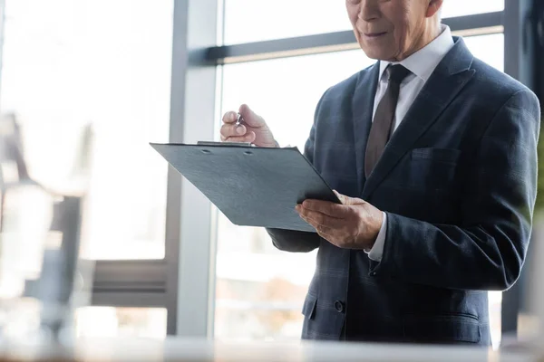 Partial view of senior businessman with clipboard and pen in office — Stock Photo