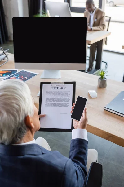 High angle view of senior businessman working with contract while holding smartphone with blank screen — Stock Photo