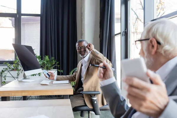 Empresário afro-americano olhando para colega sênior turvo enquanto trabalhava no escritório — Fotografia de Stock