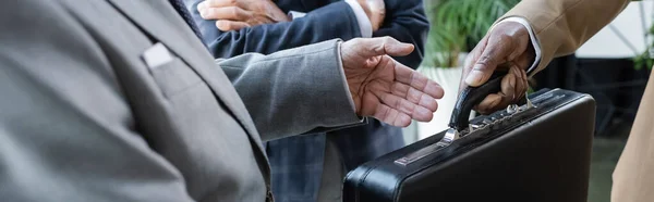 Cropped view of businessman taking briefcase from african american business partner, banner — Stock Photo