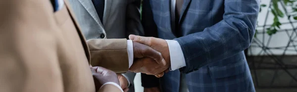 Vue recadrée d'hommes d'affaires multiethniques prospères serrant la main au bureau, bannière — Photo de stock