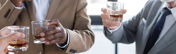 Vista parcial de hombres de negocios multiétnicos de alto nivel con vasos de whisky en la oficina, pancarta - foto de stock