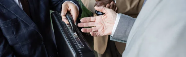 Vista parcial del hombre mayor sosteniendo maletín cerca de socios comerciales interracial, pancarta - foto de stock
