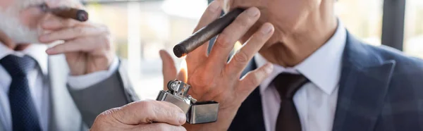 Partial view of blurred businessman lighting cigar of senior business partner, banner — Stock Photo