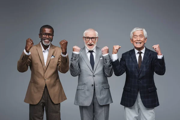 Successful multicultural businessmen showing triumph gesture isolated on grey — Stock Photo