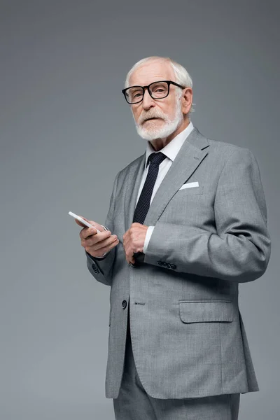 Старший уверенный в себе бизнесмен с мобильным телефоном глядя на камеру, изолированную на серый — стоковое фото