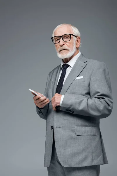 Senior confident businessman with mobile phone looking at camera isolated on grey — Stock Photo