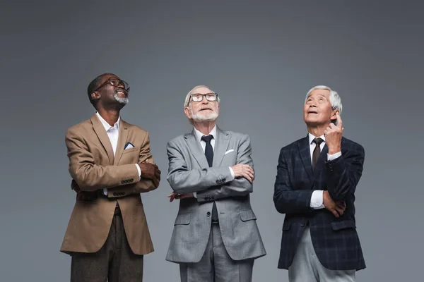 Senior asiático hombre de negocios apuntando hasta con dedo cerca multiétnico colegas aislado en gris - foto de stock