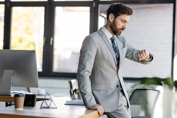 Uomo d'affari che guarda orologio da polso vicino ai computer in ufficio — Foto stock