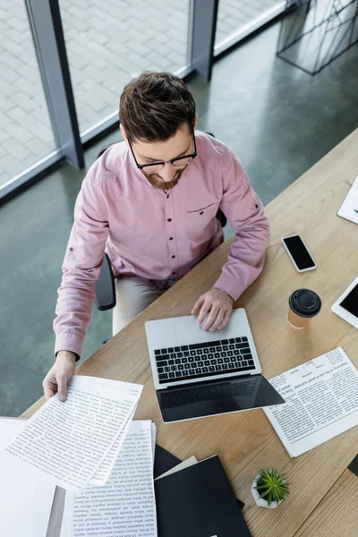 Overhead view of businessman using laptop and working with papers near coffee in office — Stock Photo