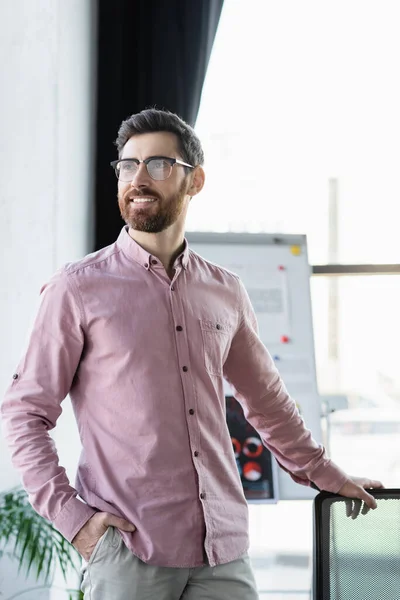 Positive businessman in eyeglasses standing in office — Stock Photo