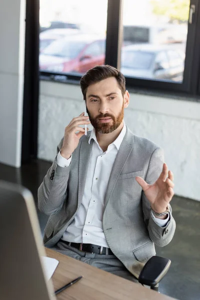 Uomo d'affari che parla su smartphone vicino al computer e notebook in ufficio — Foto stock