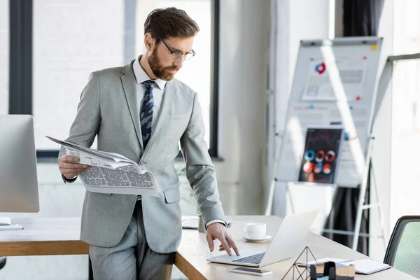 Businessman holding newspaper near laptop in office — Stock Photo