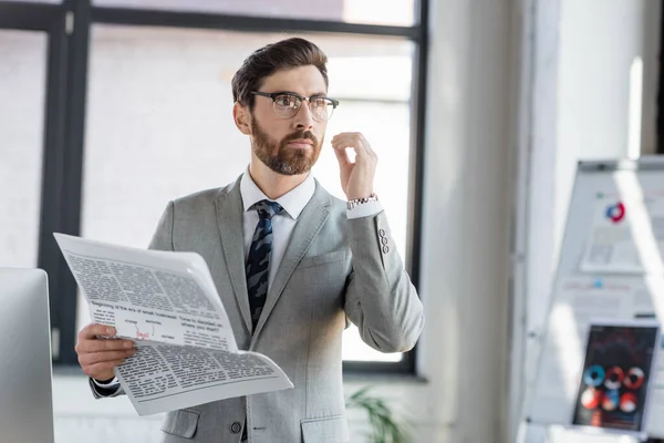 Businessman in eyeglasses holding newspaper in office — Stock Photo