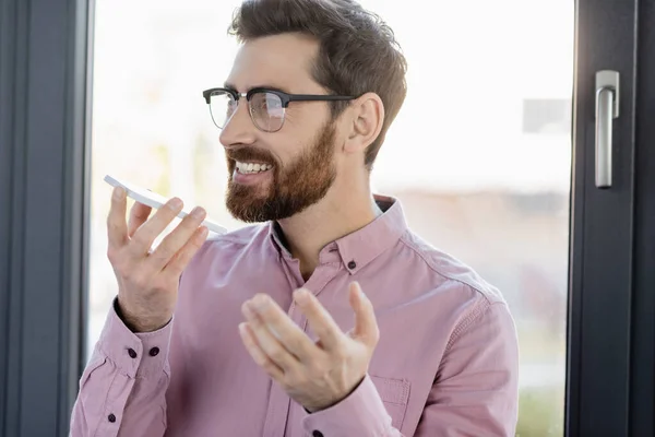 Smiling businessman recording voice message on smartphone in office — Stock Photo