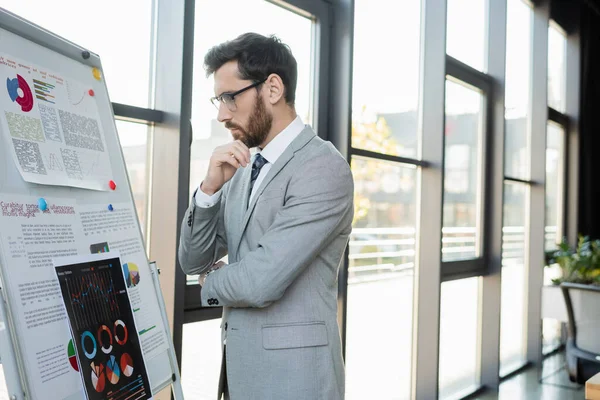 Side view of pensive businessman looking at graphs on flip chart in office — Stock Photo
