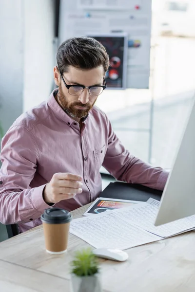 Businessman working with papers and computer near coffee to go in office — Stock Photo