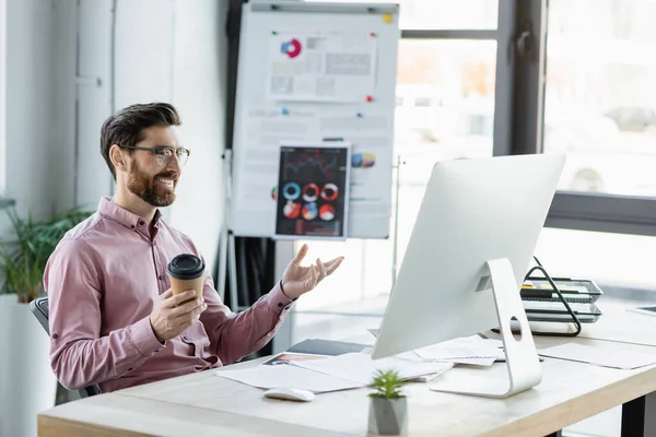 Cheerful businessman holding coffee to go near computer and documents in office — Stock Photo