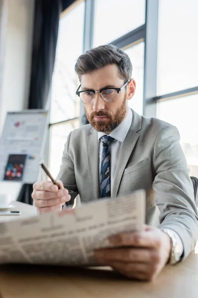 Uomo d'affari con gli occhiali che legge giornali sfocati in ufficio — Foto stock