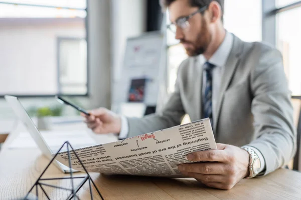 Newspaper in hand of blurred businessman working in office — Stock Photo
