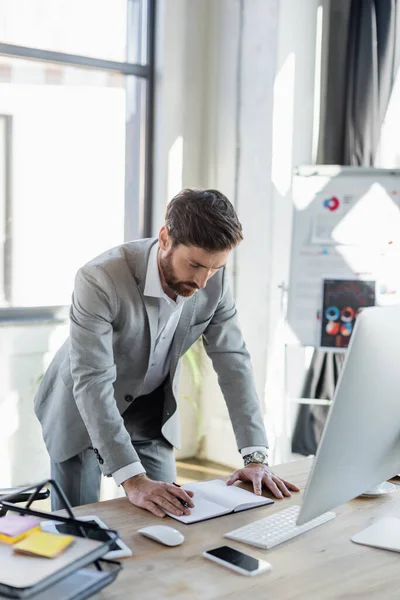 Businessman looking at notebook near devices and papers in office — Stock Photo