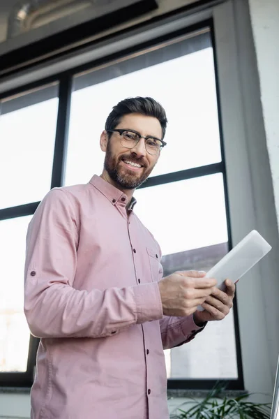 Vue à angle bas de l'homme d'affaires joyeux dans les lunettes tenant tablette numérique dans le bureau — Photo de stock