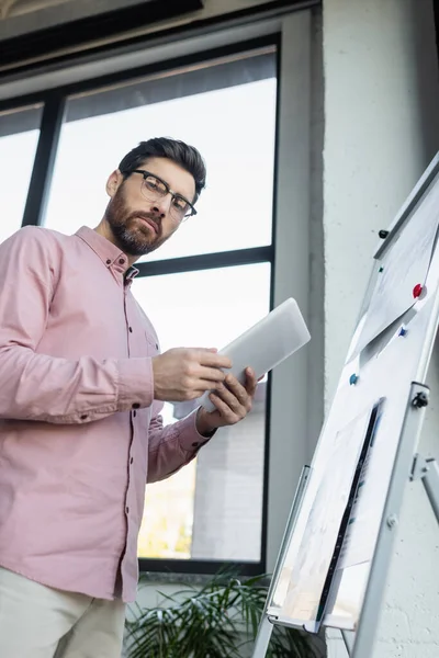 Low angle view of businessman holding digital tablet near flip chart in office — Stock Photo