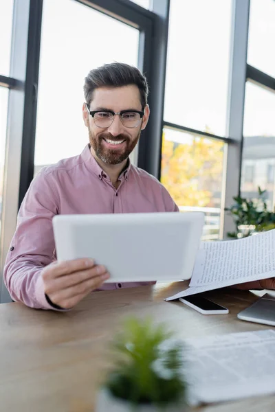 Happy businessman looking at digital tablet near papers and gadgets in office — Stock Photo