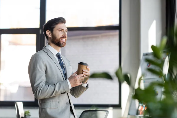 Happy businessman in suit holding coffee to go in office — Stock Photo