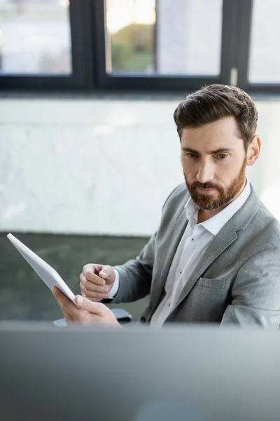 Uomo d'affari che tiene tablet digitale vicino al monitor del computer in ufficio — Foto stock