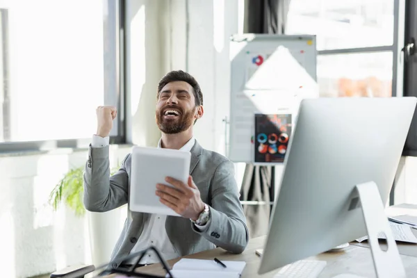 Excited businessman showing yes gesture and holding digital tablet in office — Stock Photo