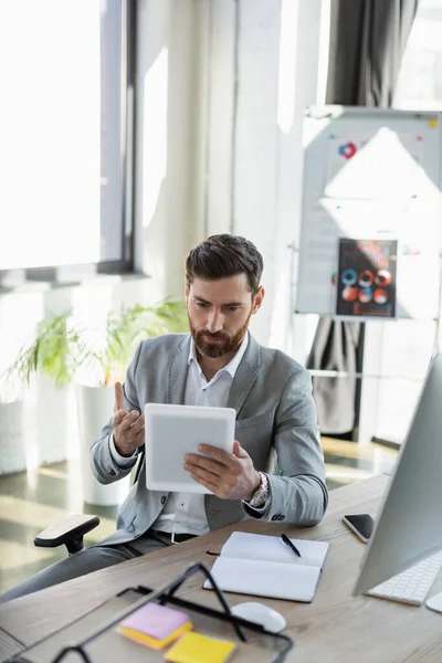 Бізнесмен вказує на цифровий планшет біля пристроїв на робочому столі в офісі — стокове фото