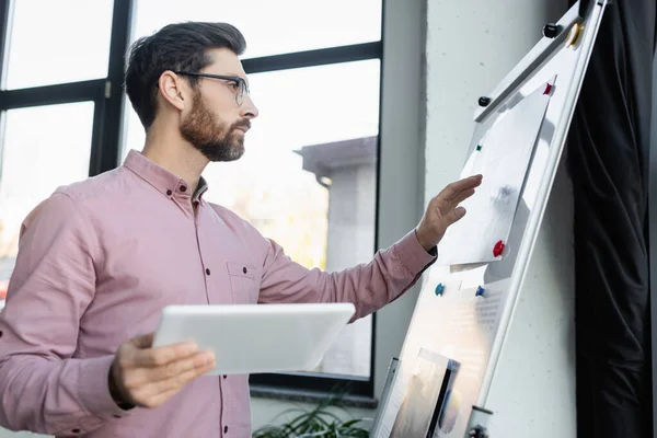 Side view of businessman holding digital tablet near flip chart in office — Stock Photo