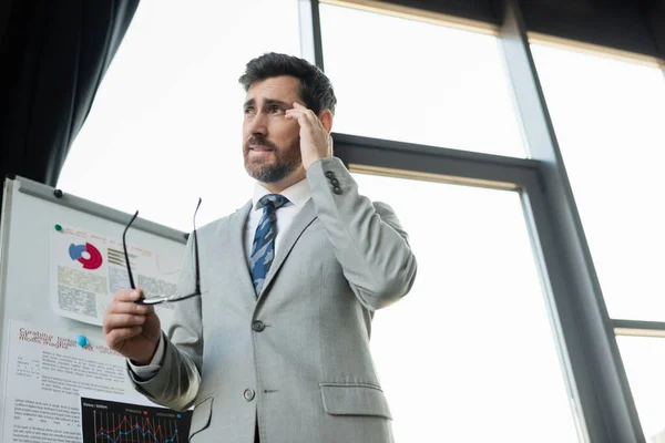 Low angle view of businessman suffering from headache near flip chart in office — Stock Photo